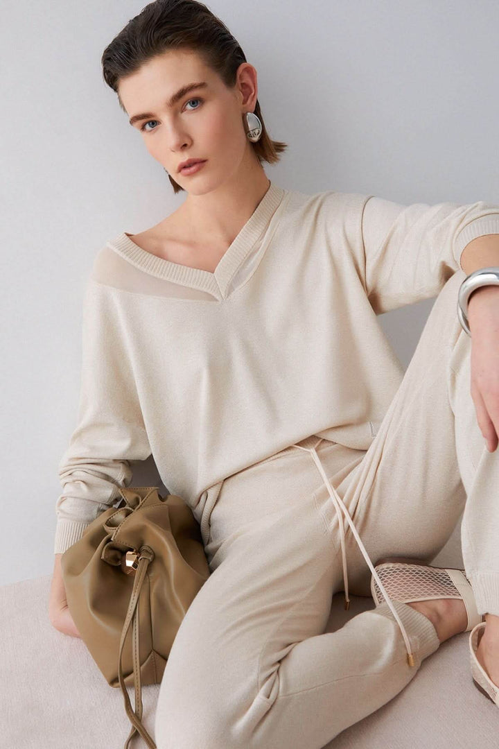 Femme portant un tricot col en V à manches longues, tissu doux et léger, avec un sac beige, tenue élégante et décontractée.