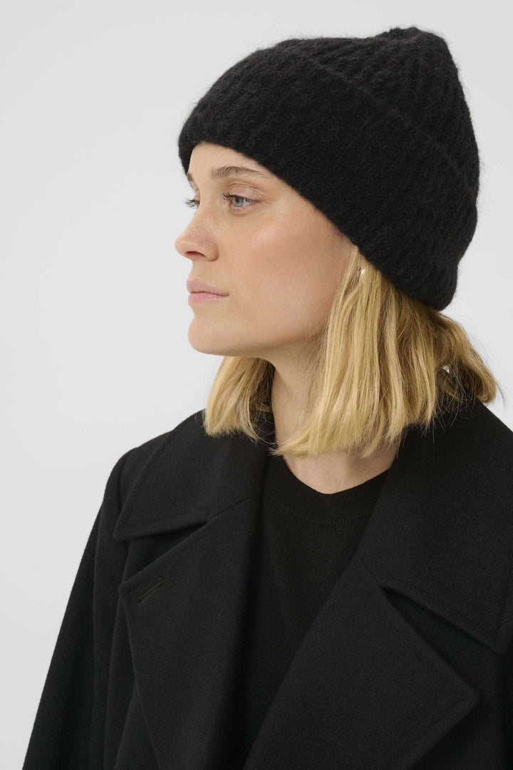 Femme portant une tuque Sanja noire en tricot côtelé, style hivernal moderne et décontracté.