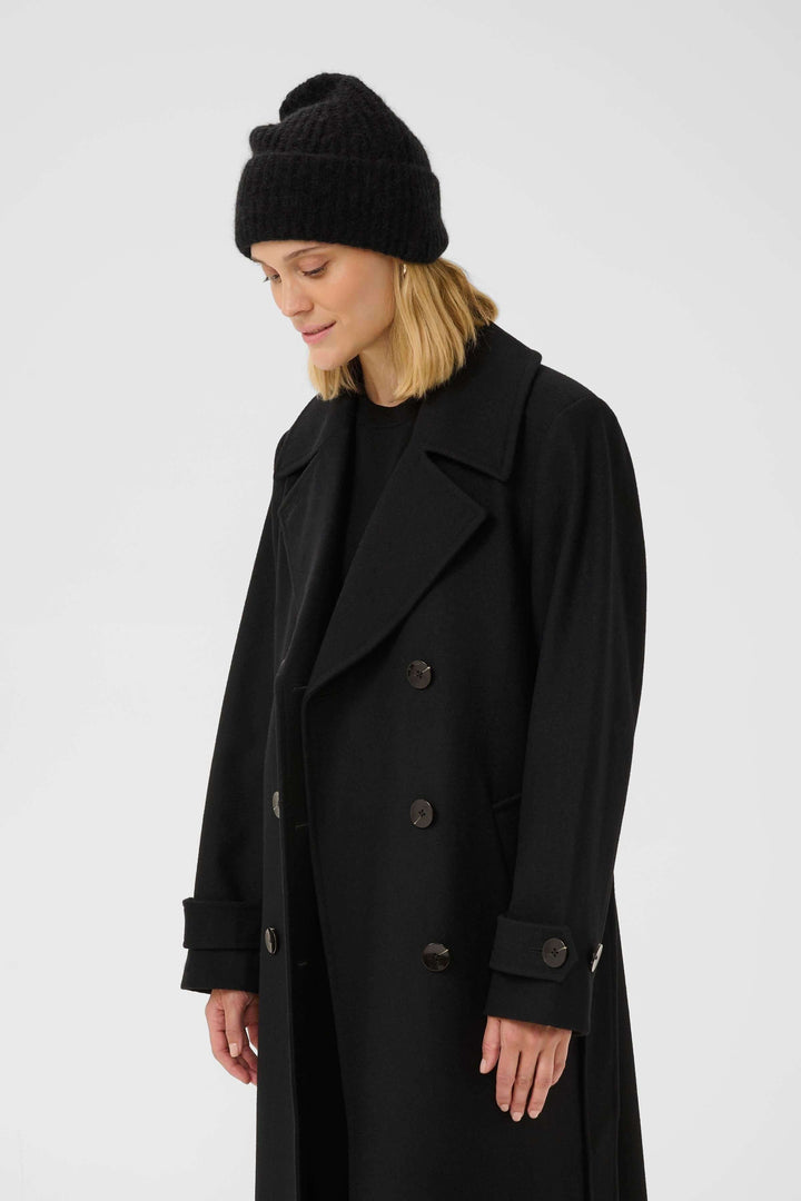 Person wearing a black ribbed knit tufted tuque and black coat, showcasing a modern casual winter style.