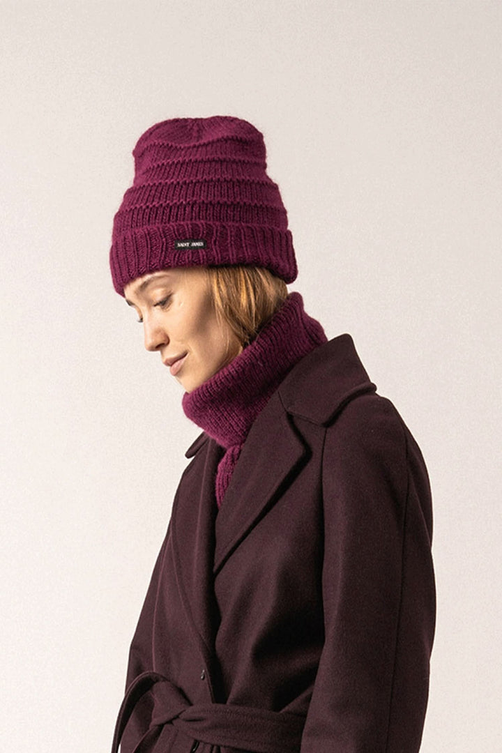 Femme portant une tuque prune élégante avec une étiquette discrète, associée à un col pour un look hivernal chic.