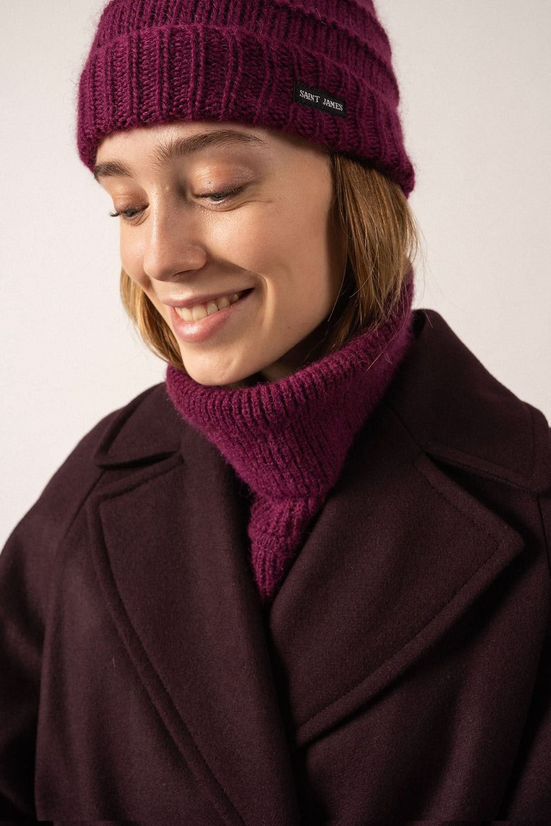 Femme souriante portant une tuque prune tricotée et un col assorti, élégante pour l'hiver.