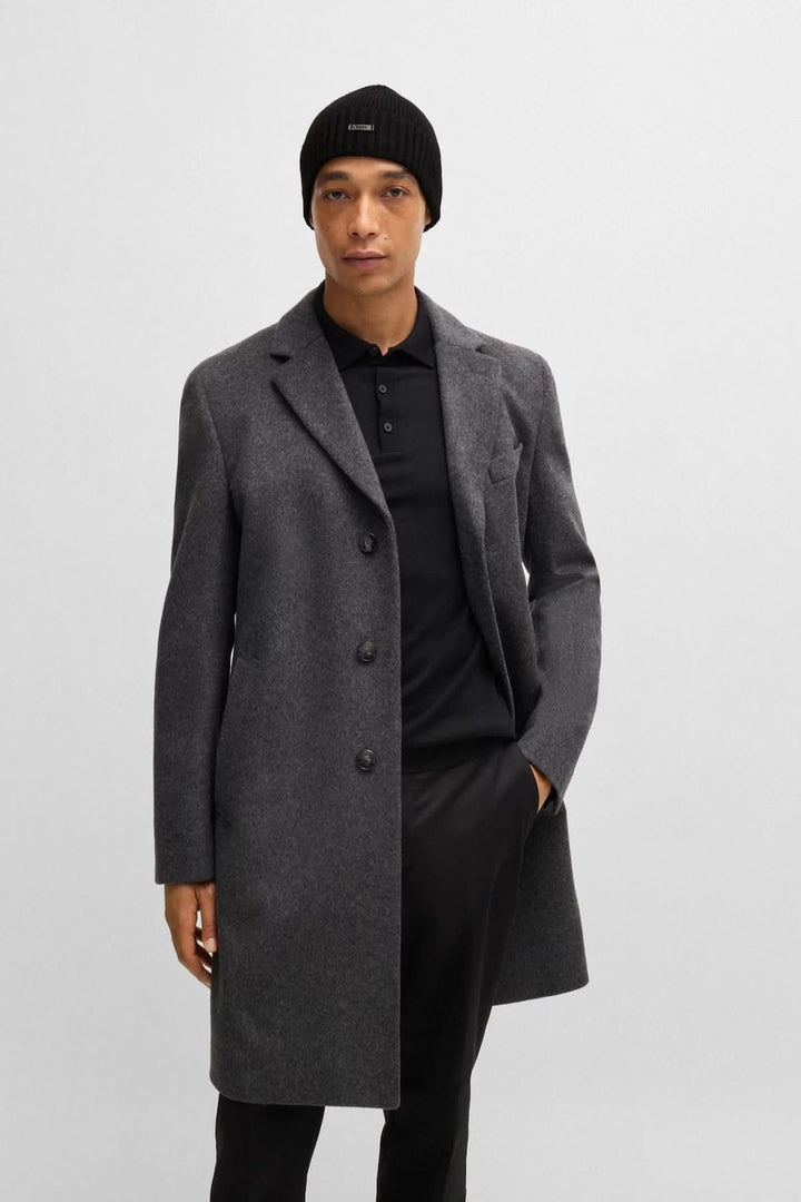 Homme portant un manteau gris et un bonnet noir, look élégant décontracté.