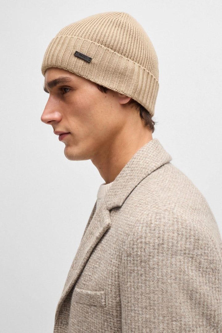 Bonnet en laine beige avec une étiquette logo, porté par un homme en manteau élégant.