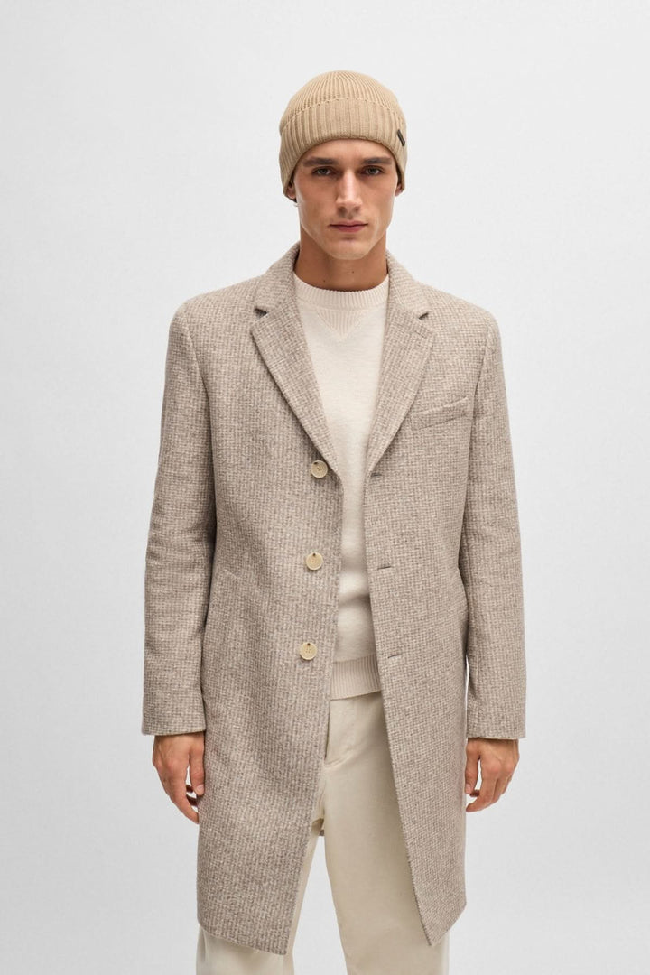 Homme portant un manteau beige avec un bonnet en laine, style élégant pour un look moderne.