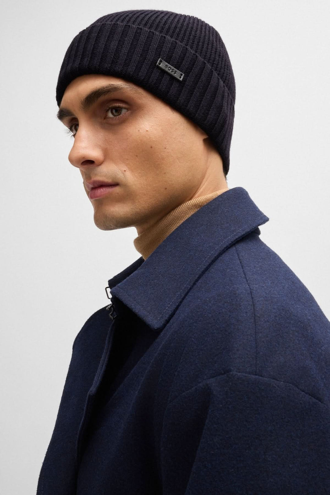 Homme portant une tuque de laine noire à côtes avec étiquette en tissu BOSS, vêtu d'un manteau bleu.