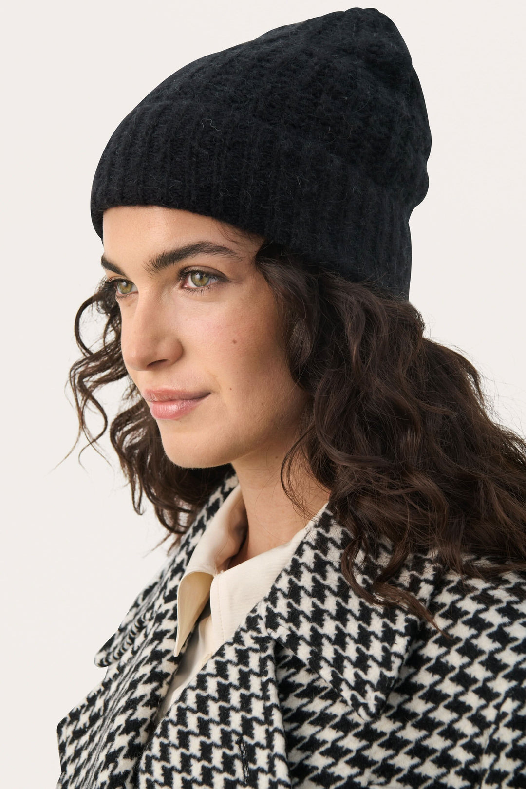 Modèle portant une tuque moelleuse Micha, en tricot noir, avec un manteau à motifs classiques.