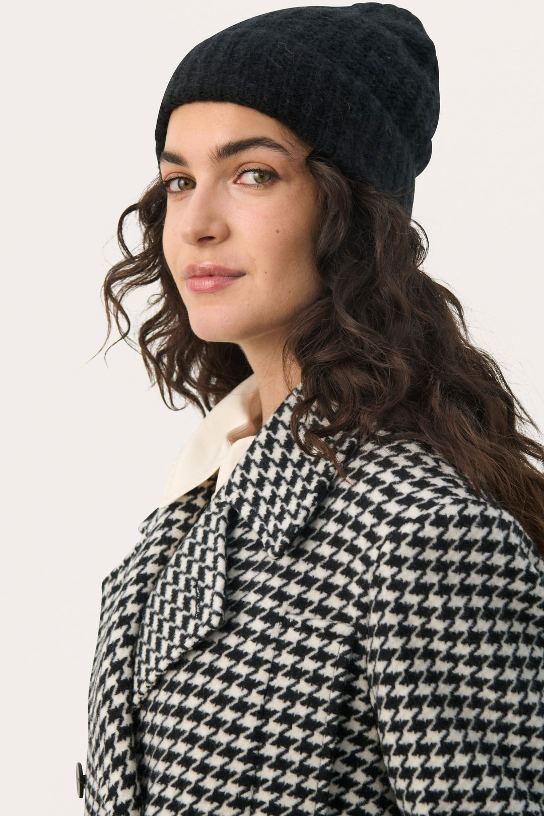 Femme portant une tuque moelleuse Micha, avec un manteau à motifs écossais, pour une allure chic et décontractée.