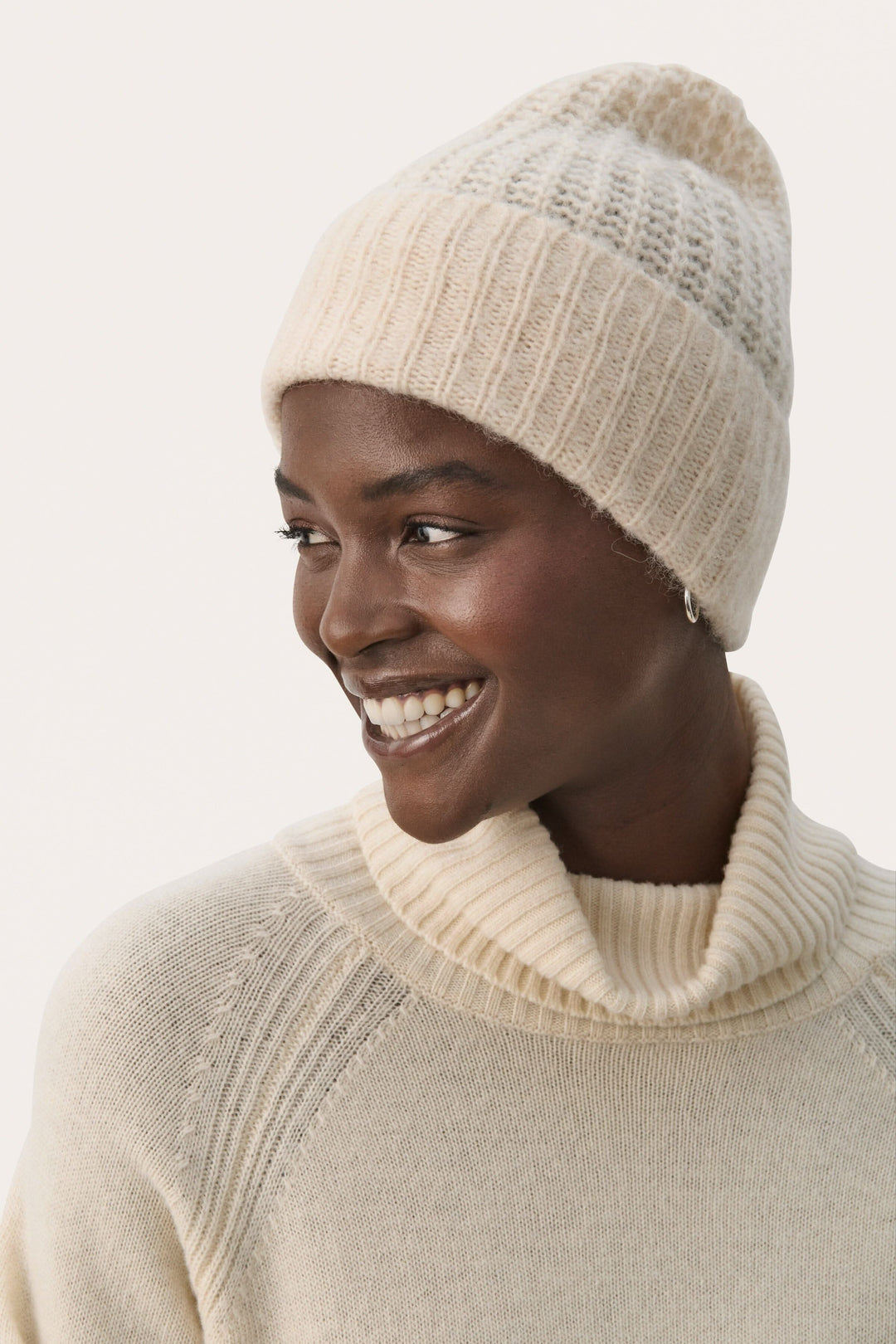 Femme souriante portant une tuque moelleuse beige et un pull à col roulé, parfaite pour les journées froides.