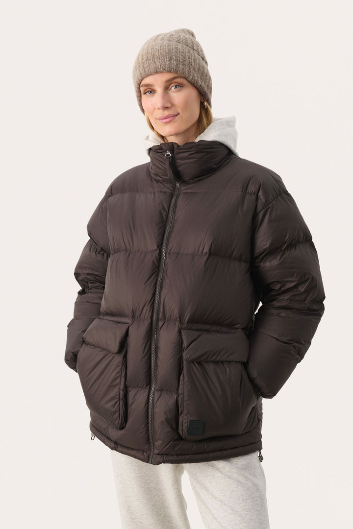 Femme souriante portant une doudoune noire avec poches et un bonnet beige, parfait pour les journées froides.