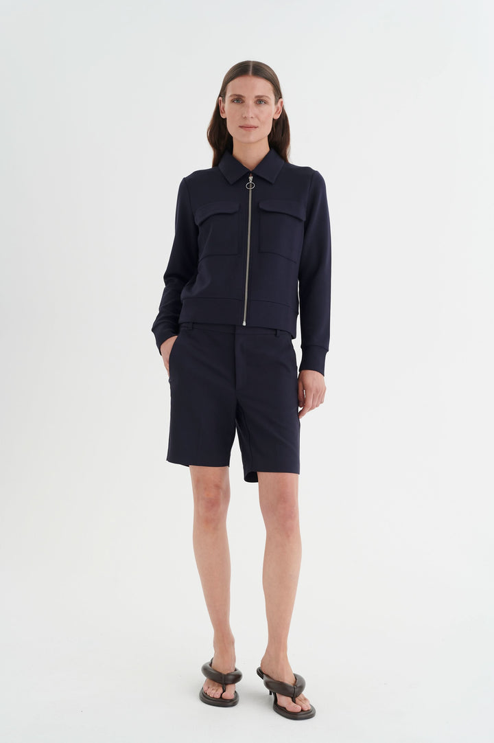 Veste Beca à manches longues, fermeture éclair, poches poitrine, associée à un short, look chic et urbain.