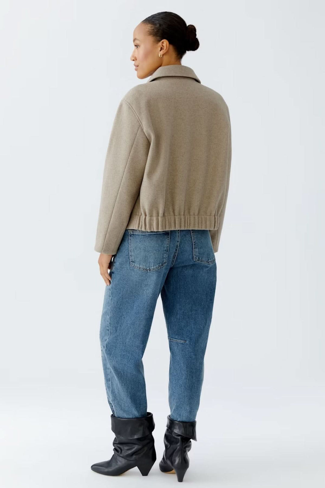 Femme portant une veste à coupe droite avec col classique, matière douce et fermeture à boutons, sur un jean et bottes noires.