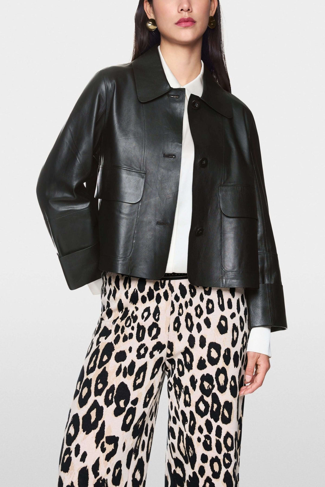 Veste coupe moderne en cuir noir avec col classique et grandes poches, portée sur chemise blanche et pantalon imprimé léopard.