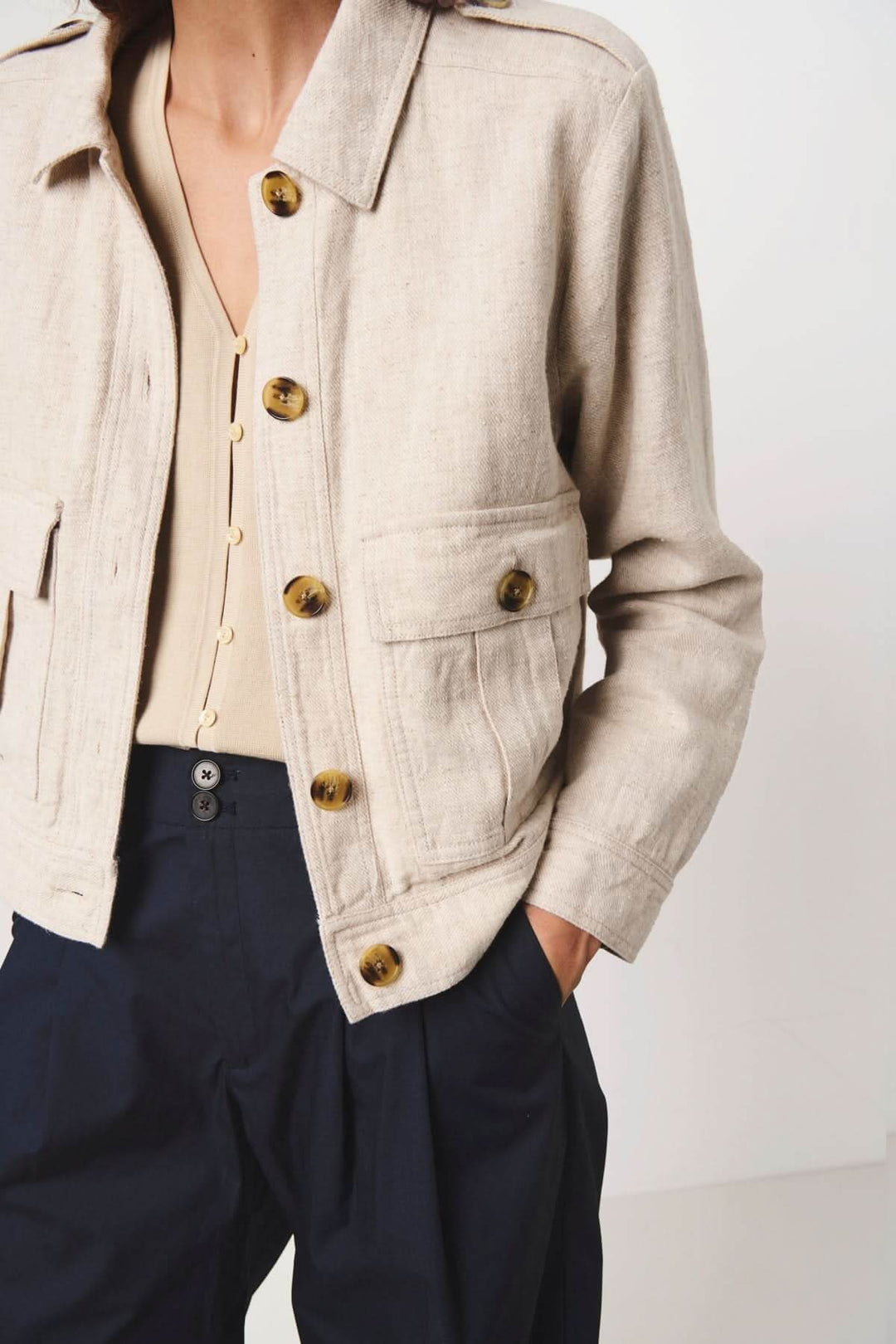 Veste courte Najah en lin beige avec manches longues et grandes poches avant, boutonnières dorées et détails élégants.