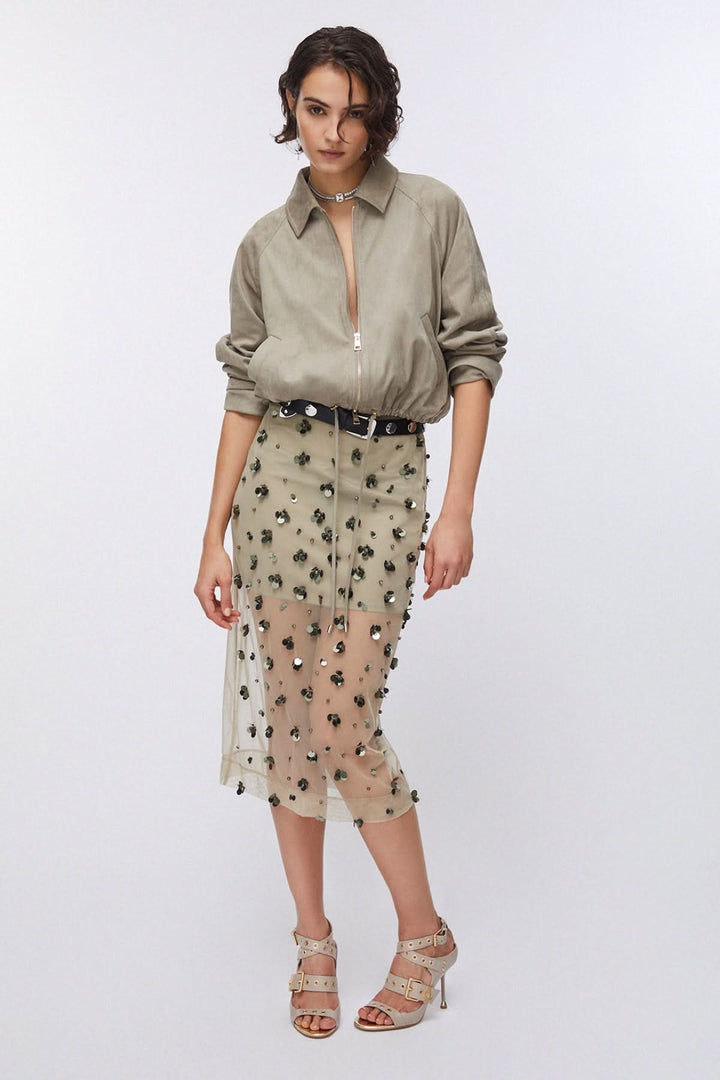 Femme portant une Veste courte zippée à col chemise moderne et jupe transparente ornée, look élégant et tendance pour la saison.
