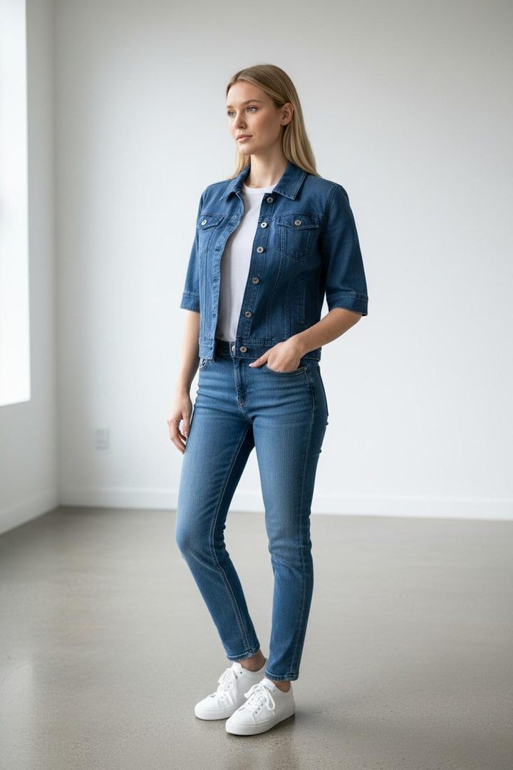 Veste en denim manches courtes avec coupe moderne et manches revers pour un look estival, portée par un mannequin dans une pièce lumineuse.