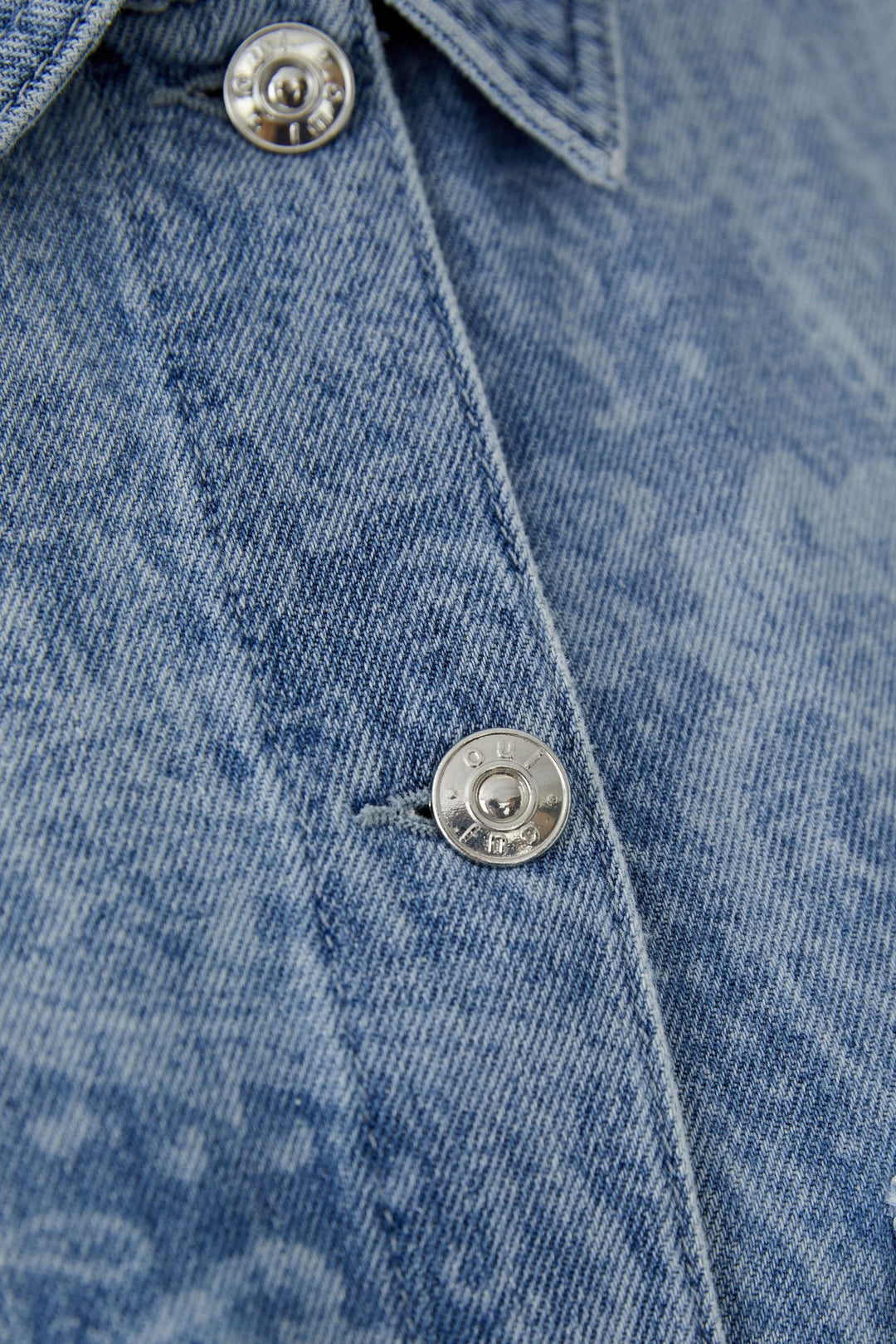 Veste en jean imprimée avec motif cachemire subtil et fermeture boutonnée en gros plan, col classique visible.