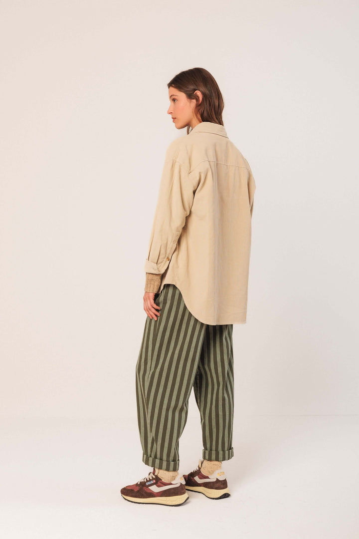 Femme portant une veste en velours côtelé beige avec un pantalon rayé vert, style décontracté et moderne.
