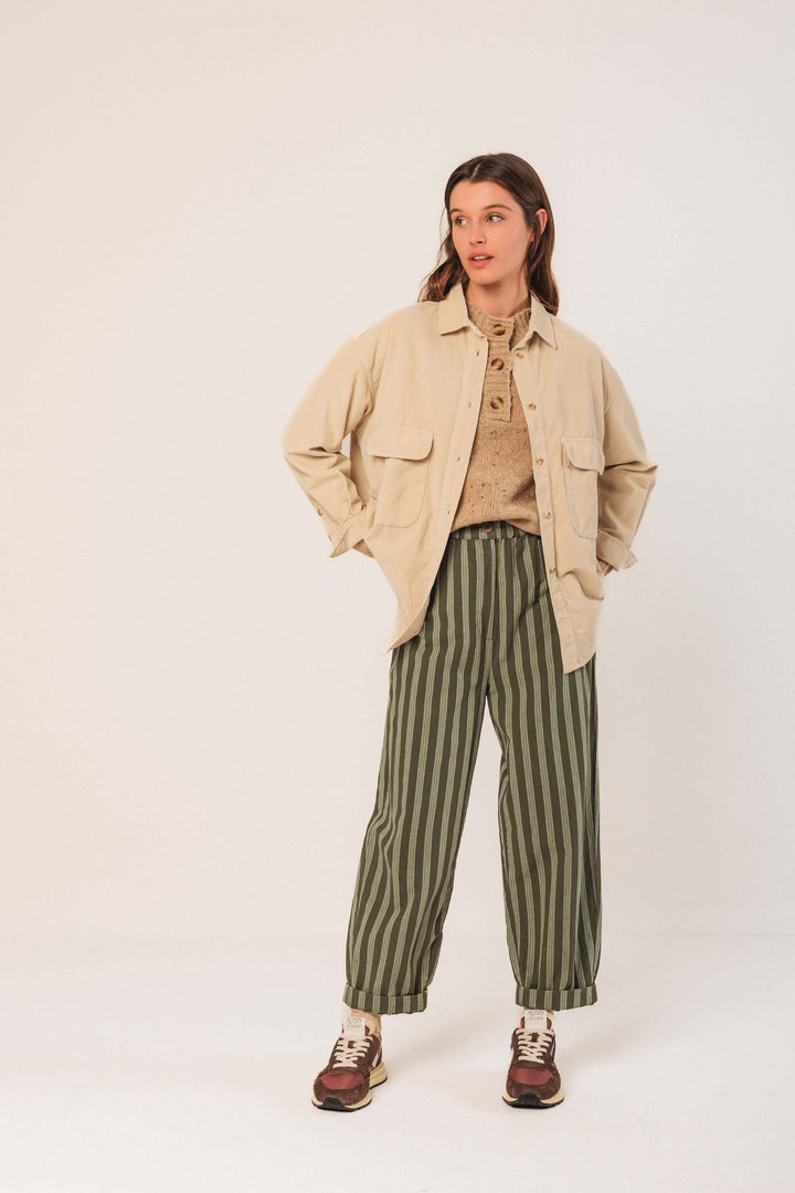 Femme portant une veste en velours côtelé beige avec un pantalon à rayures vertes, style décontracté et tendance.