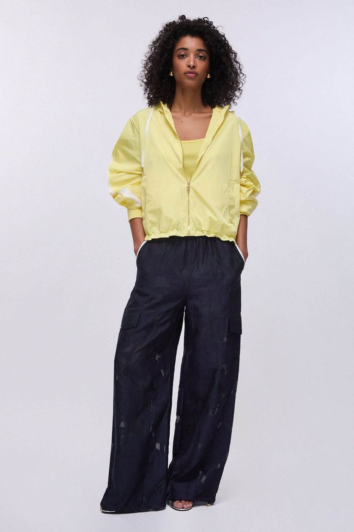 Veste légère à capuche zippée jaune portée par une femme, avec pantalon large, style décontracté et moderne.