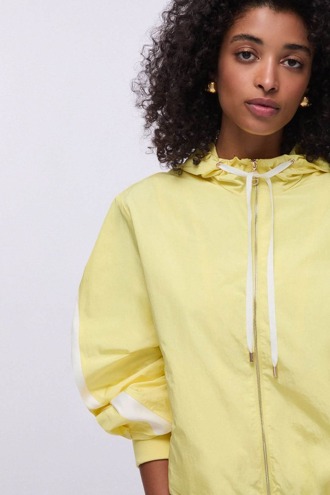 Femme portant une veste légère à capuche zippée jaune, idéale pour un look urbain décontracté.