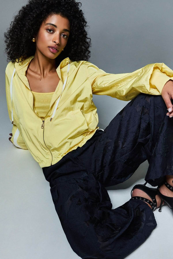 Femme portant une veste légère à capuche zippée jaune avec un pantalon noir, style moderne et décontracté pour la mi-saison.