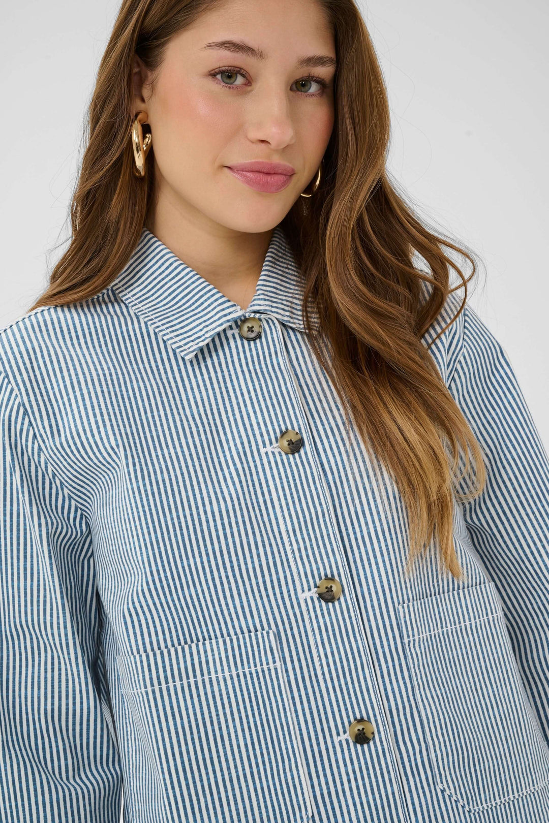 Femme portant une veste légère rayée à boutons avec col chemise et poches avant, manches longues et coupe courte.