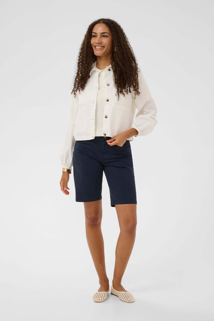 Femme portant une veste légère rayée à boutons avec un short bleu, créant un look moderne et décontracté.