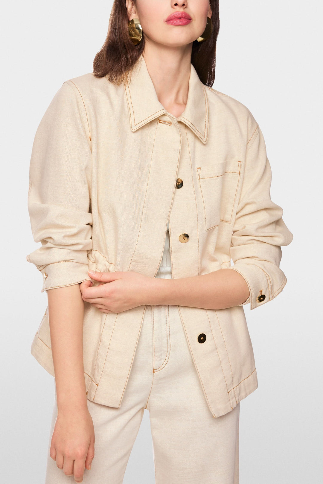 Femme portant une veste légère à taille ajustable avec détails utilitaires et col chemise structuré, tenue moderne et épurée.