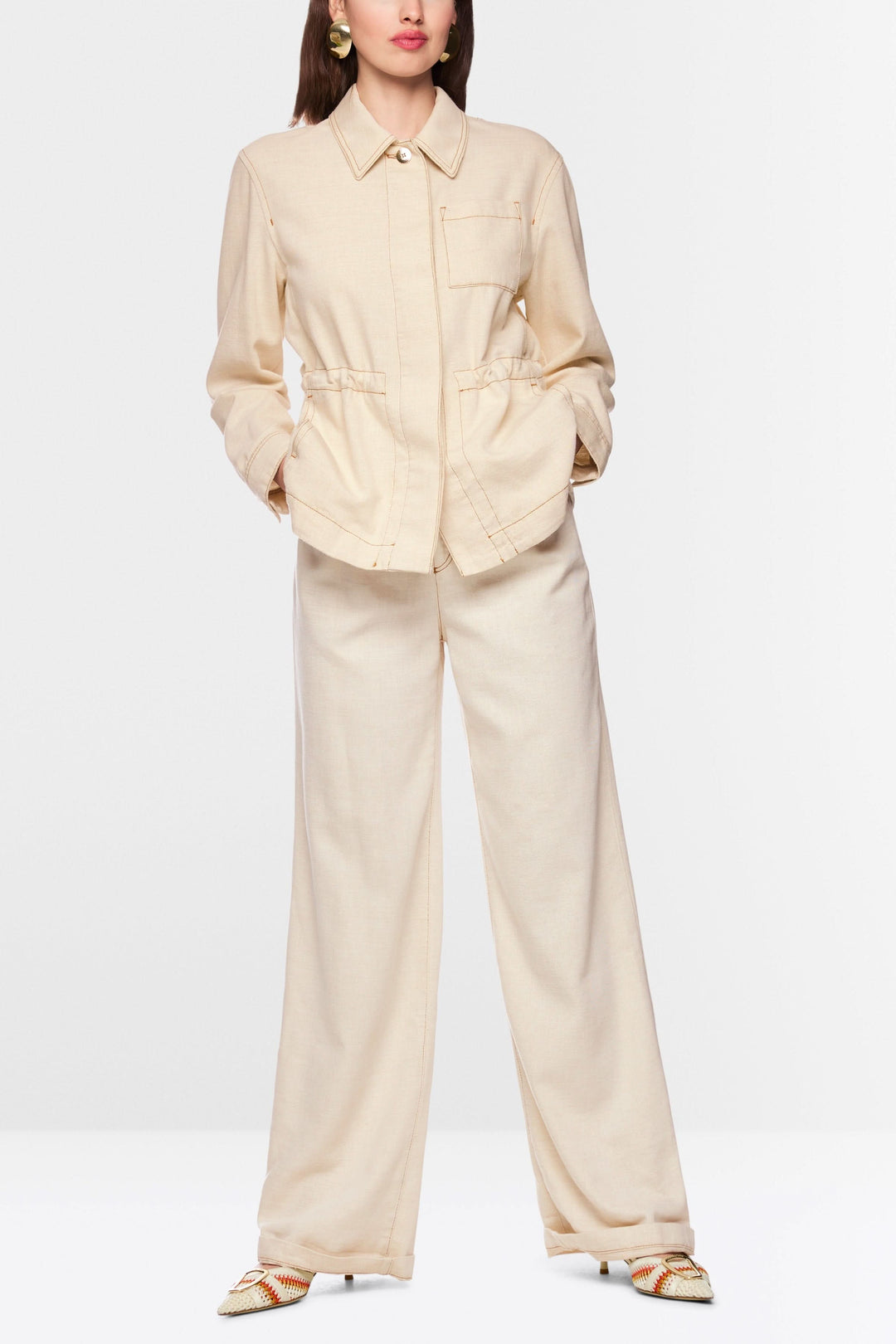 Veste légère à taille ajustable avec col chemise structuré, boutons et cordon à la taille, portée avec pantalon beige ample.