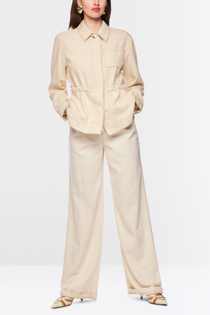 Veste légère à taille ajustable avec col chemise structuré, boutons et cordon à la taille, portée avec pantalon beige ample.