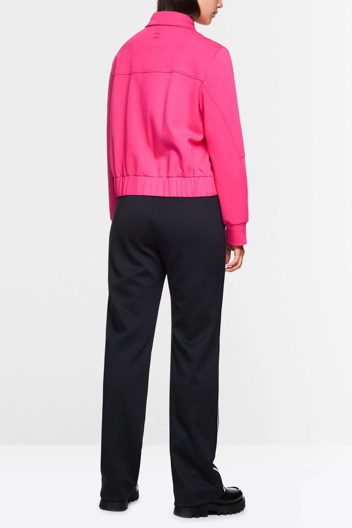 Femme vue de dos portant une veste moderne rose avec pantalon noir, style décontracté et contemporain.
