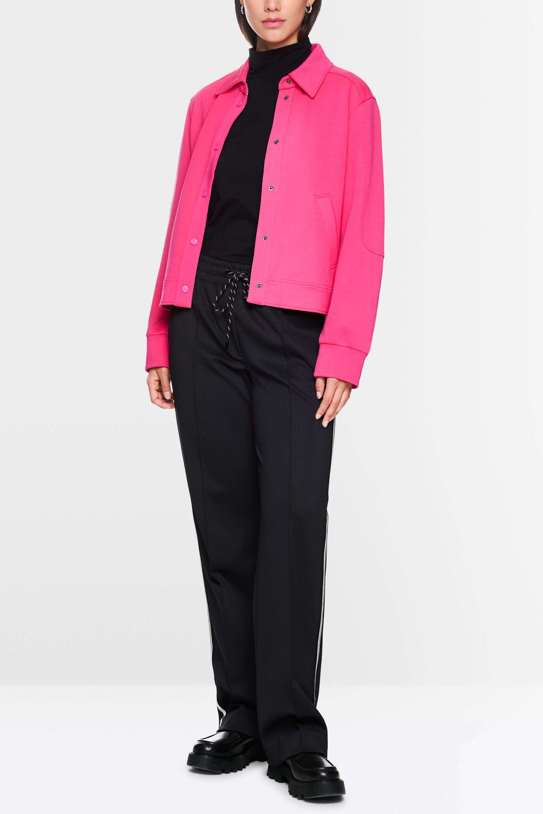 Veste moderne rose portée avec un t-shirt noir et un pantalon noir, affichant un style décontracté et tendance.