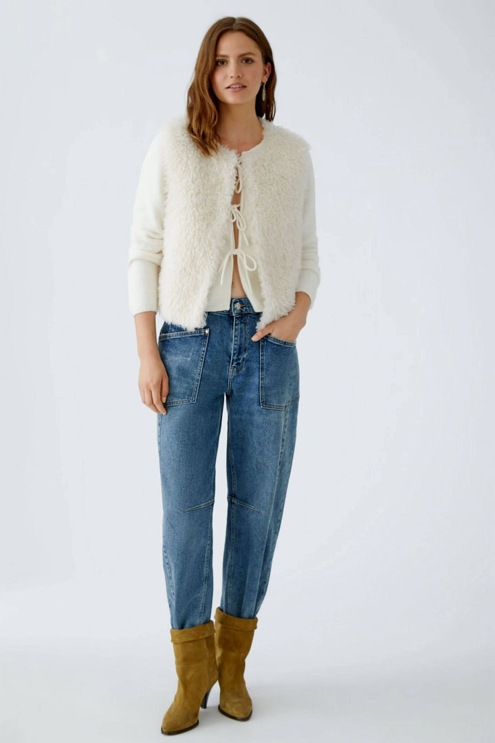 Veste sans manches en fausse fourrure blanche associée à un jean décontracté et des bottes jaunes.