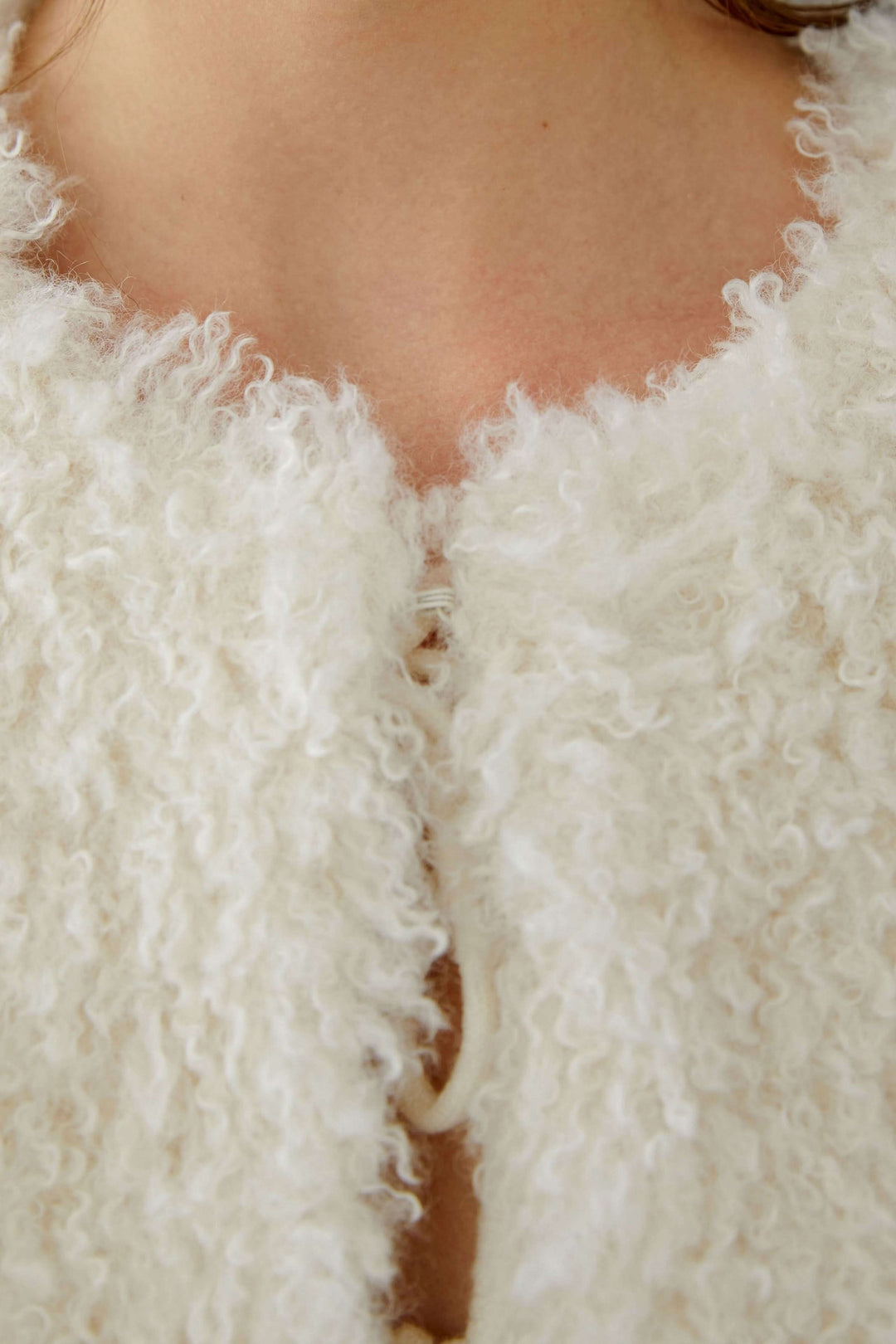 Gros plan sur la veste sans manches en fausse fourrure, mettant en valeur sa texture douce et sa fermeture par crochets.