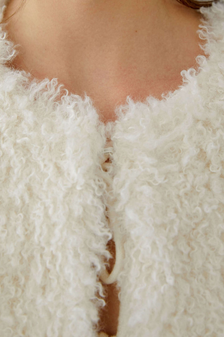 Gros plan sur la veste sans manches en fausse fourrure, mettant en valeur sa texture douce et sa fermeture par crochets.