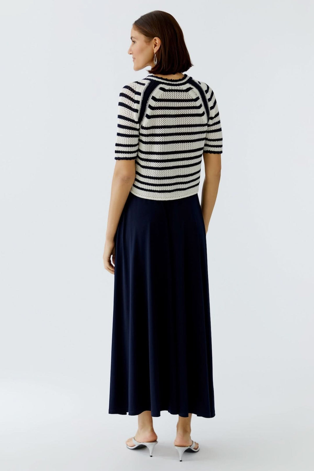 Veste tricot à rayures avec bordures contrastantes sur une femme élégante, vue de dos, avec jupe longue.
