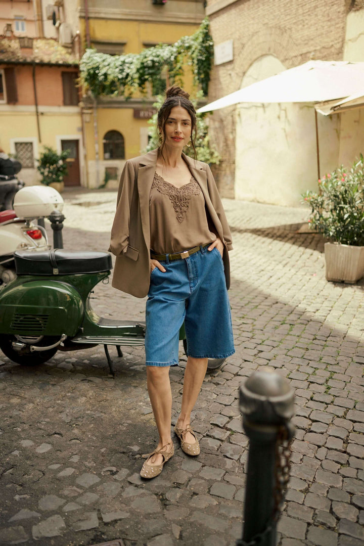 Femme portant un veston décontracté avec un top et un short en denim dans une ruelle pittoresque.