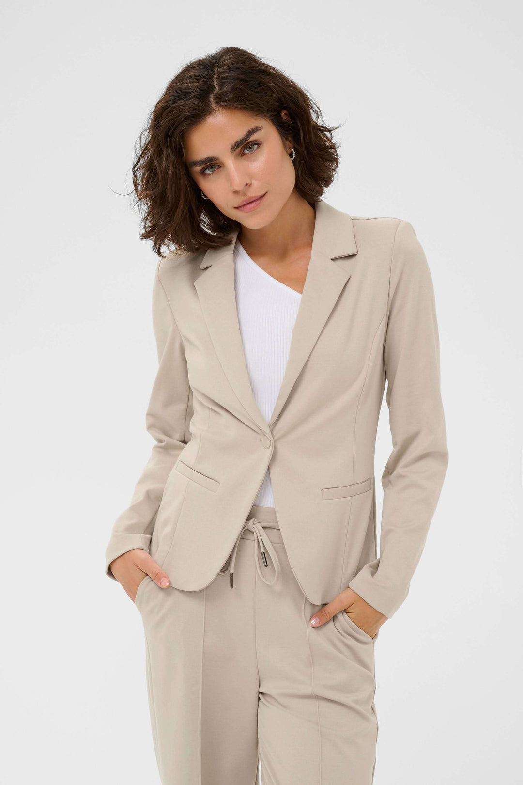 Femme portant le Veston Jenny ajusté avec col tailleur beige, tenue élégante et féminine pour un look quotidien soigné.