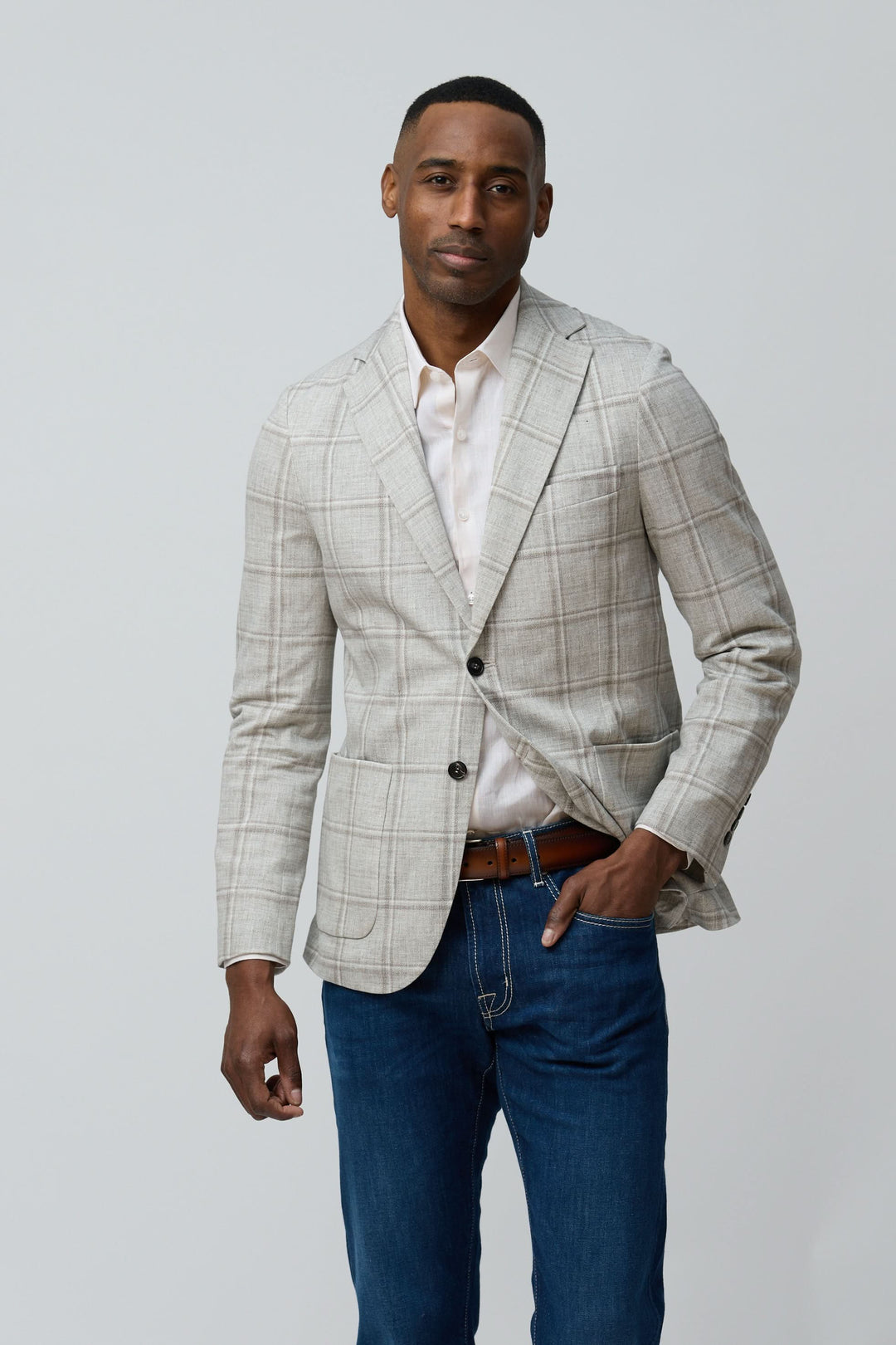 Homme portant un veston à carreaux texturés avec une chemise blanche et un jean, casual mais élégant.