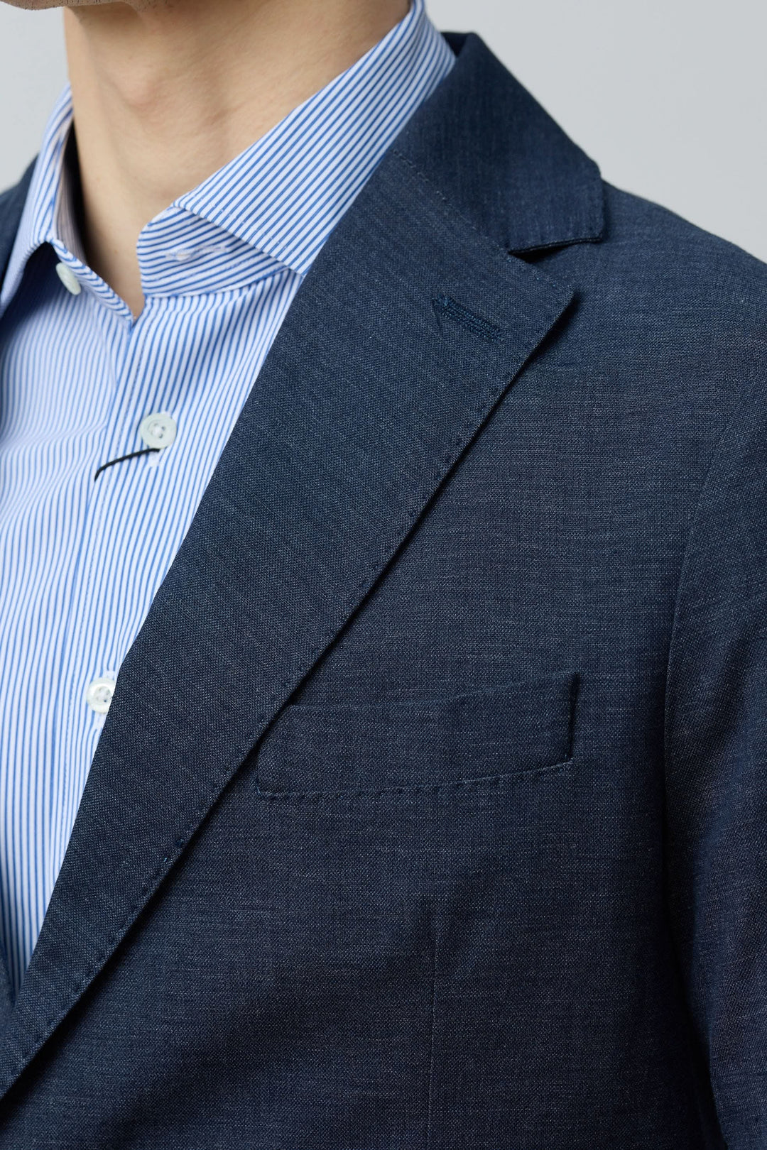 Veston en coton et lin extensible, coupe ajustée avec revers classique, porté sur chemise à rayures bleues.
