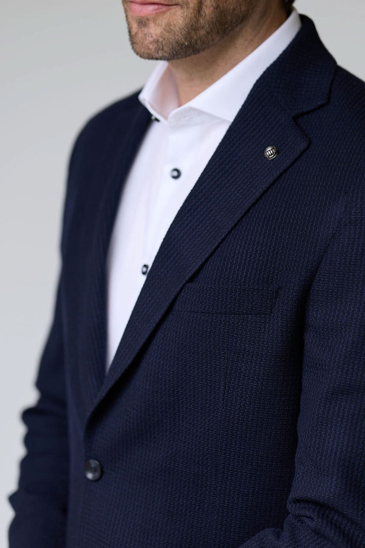 Veston en tricot structuré porté avec une chemise blanche, offrant élégance et confort grâce à sa matière texturée et souple.