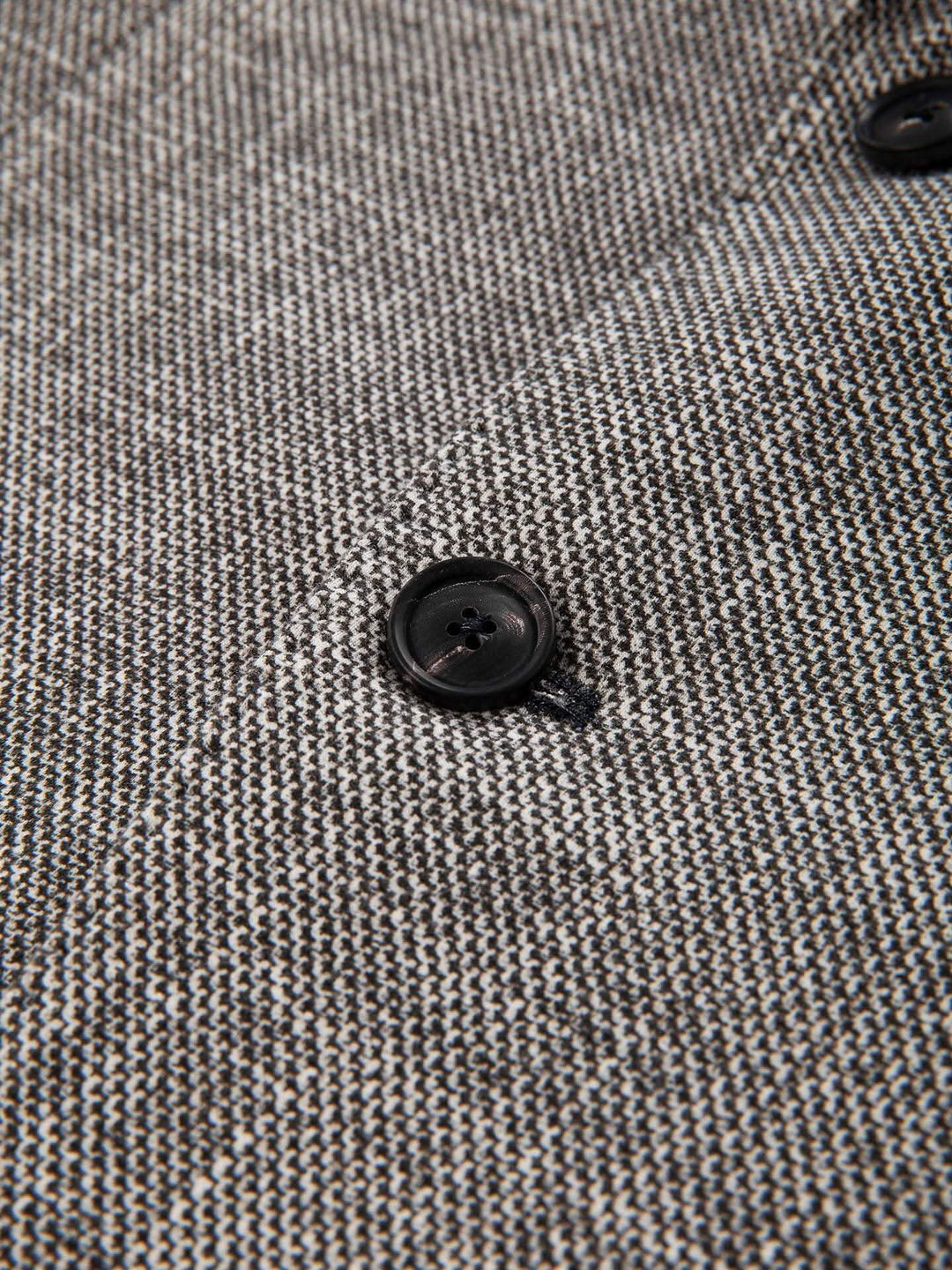 Détail du veston texturé avec bouton en corne et texture raffinée.
