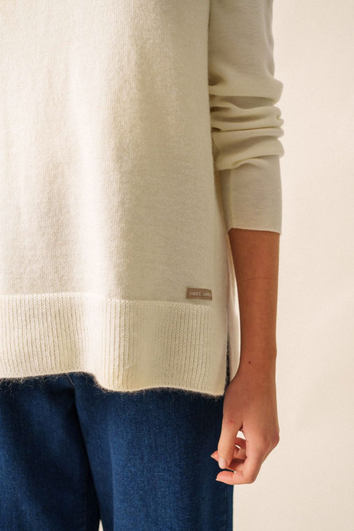 Veste sans manche en jersey crème avec détails côtelés et logo, portée avec un jean bleu, style décontracté.