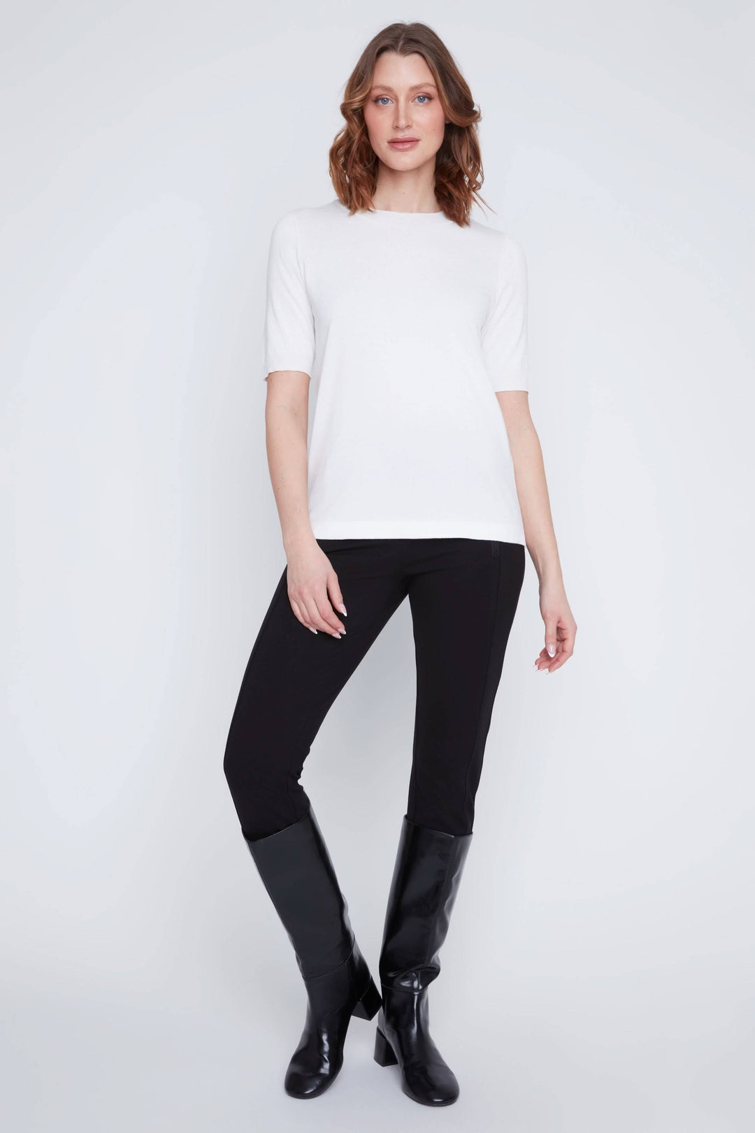 Femme portant un t-shirt classique blanc avec un pantalon noir et des bottes, style minimaliste et élégant.
