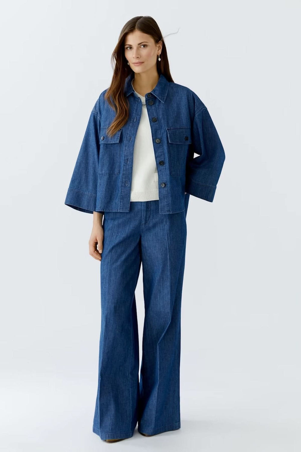 Femme portant une veste courte en denim avec manches larges et pantalon assorti, style moderne et décontracté.