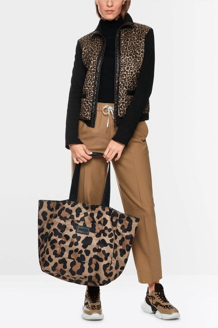 Femme portant une veste avec manche imprimée, pantalon beige, avec un grand sac cabas léopard, style moderne et pratique.