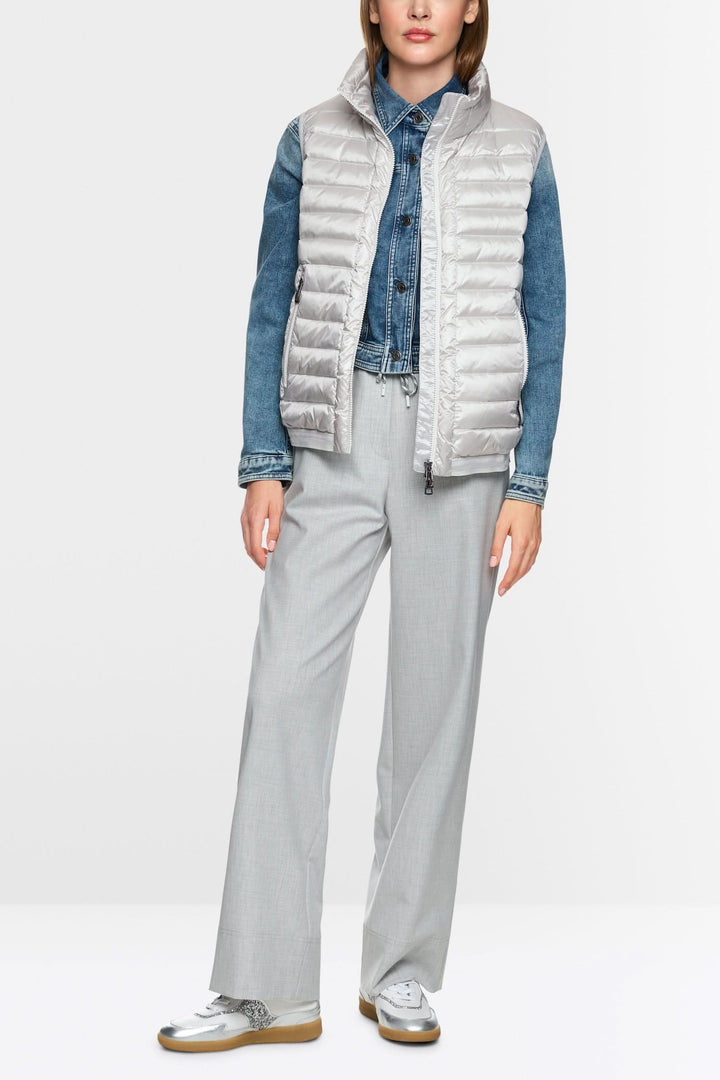 Femme portant une veste matelassée sans manches, jean en denim et pantalon gris élégant, style contemporain.