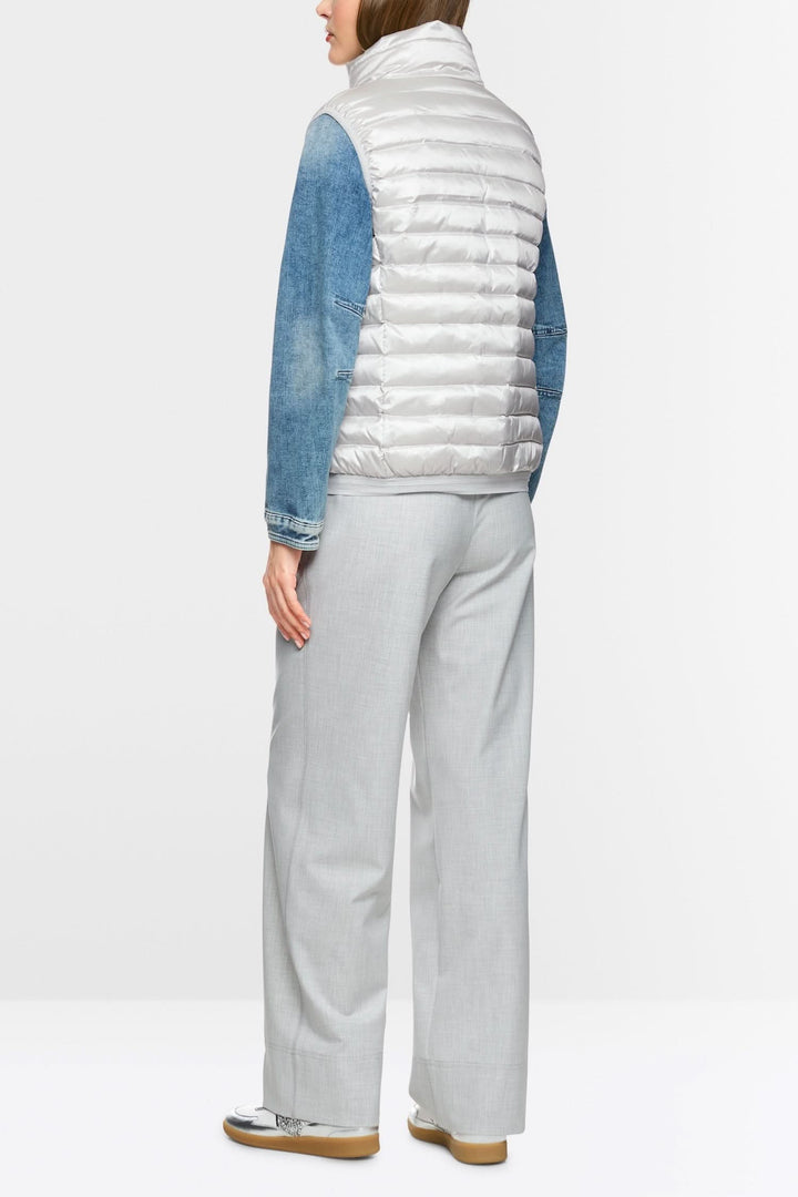 Femme portant une veste matelassée sans manches, vue arrière, associée à un pantalon léger.