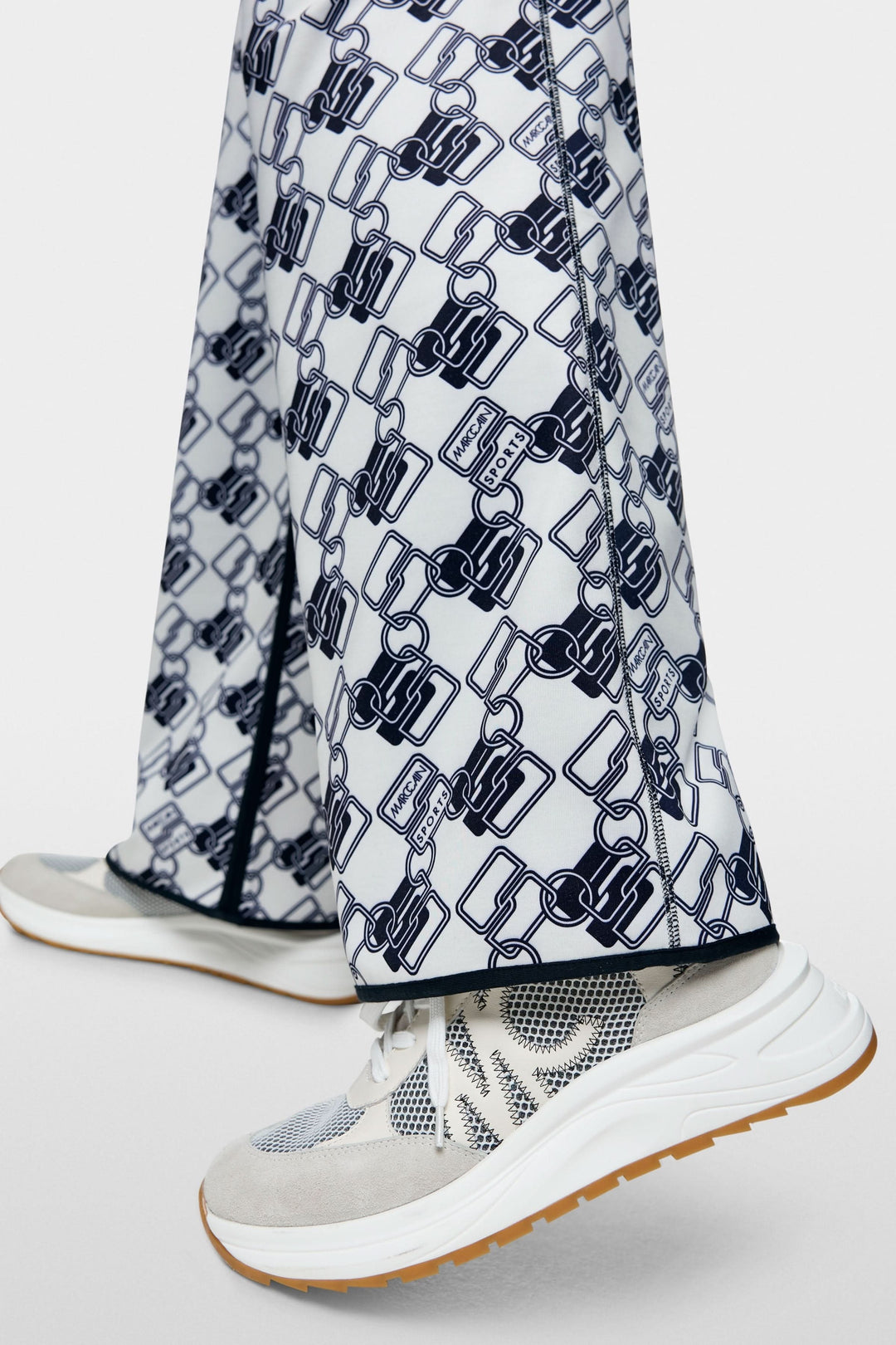Pantalon de jogging réversible Washington avec motif graphique maillons entrelacés, porté avec des baskets sportives.