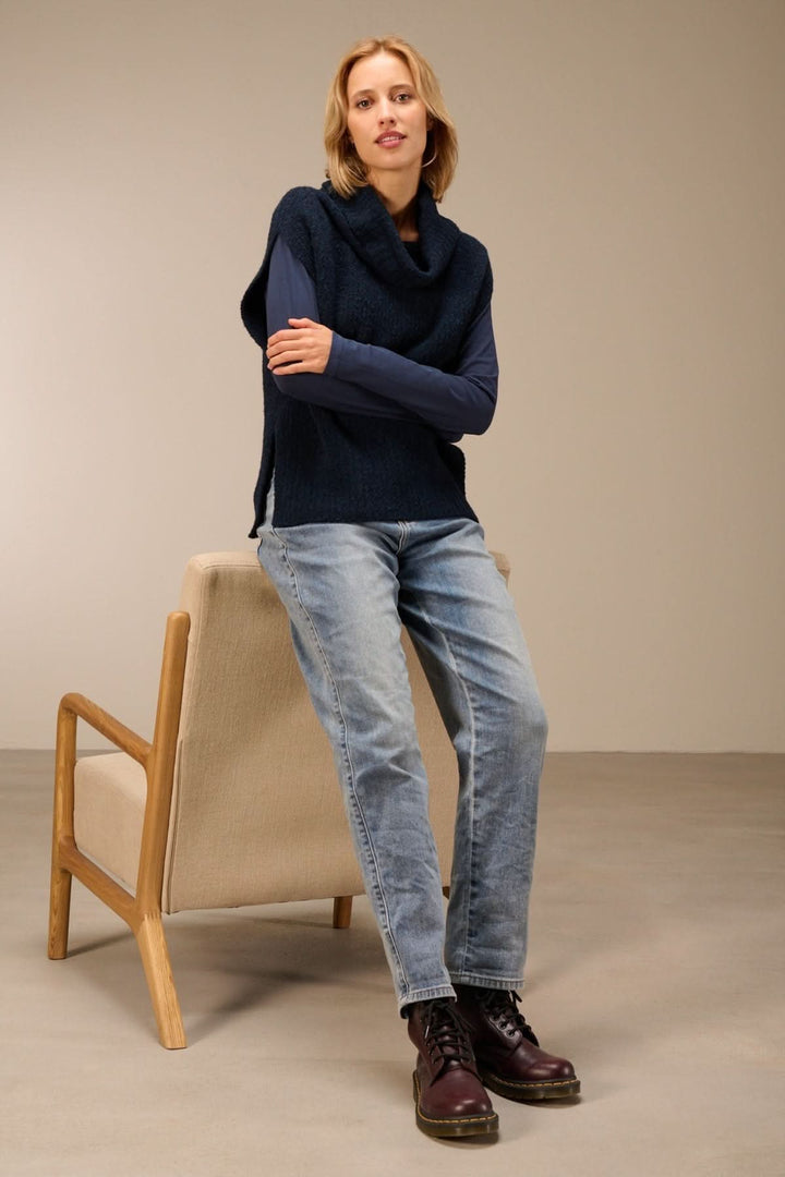 Femme portant un gilet sans manches en maille bouclée à col drapé, style décontracté avec t-shirt à manches longues et jeans.